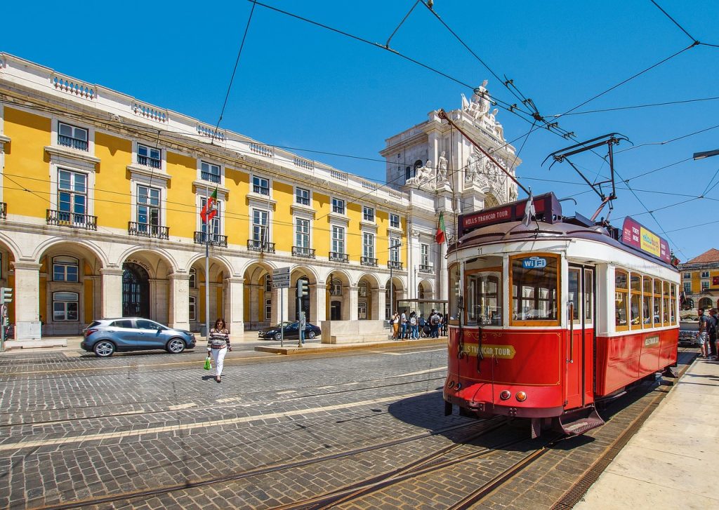 Tranvía rojo en Lisboa frente a edificio porticado de color amarillo